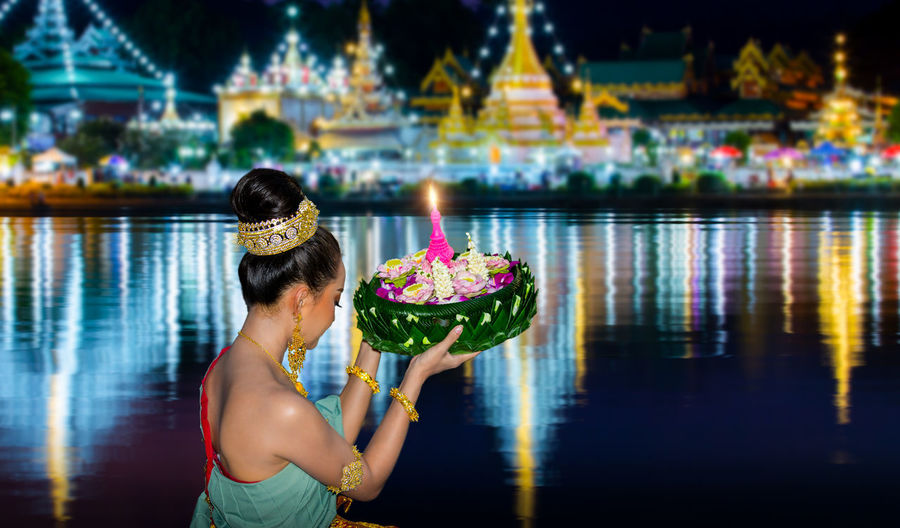 Side view of woman wearing traditional clothing holding religious offering by lake