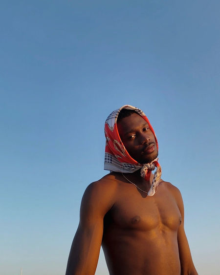 Low angle view of shirtless man against clear blue sky