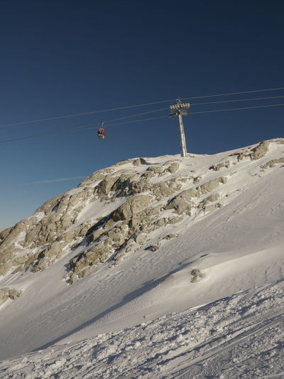 Low angle view of overhead cable car on snow covered mountain against clear sky