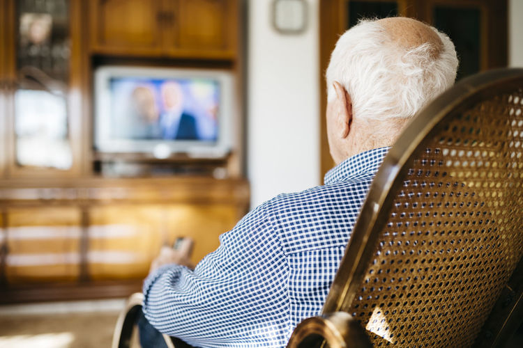Back view of senior man sitting in his rocker watching television