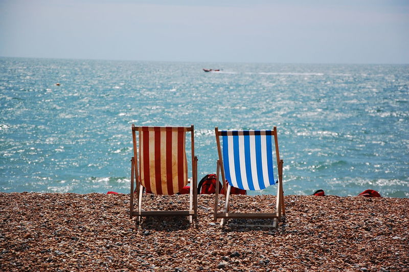 Empty folding chairs on shore against clear sky