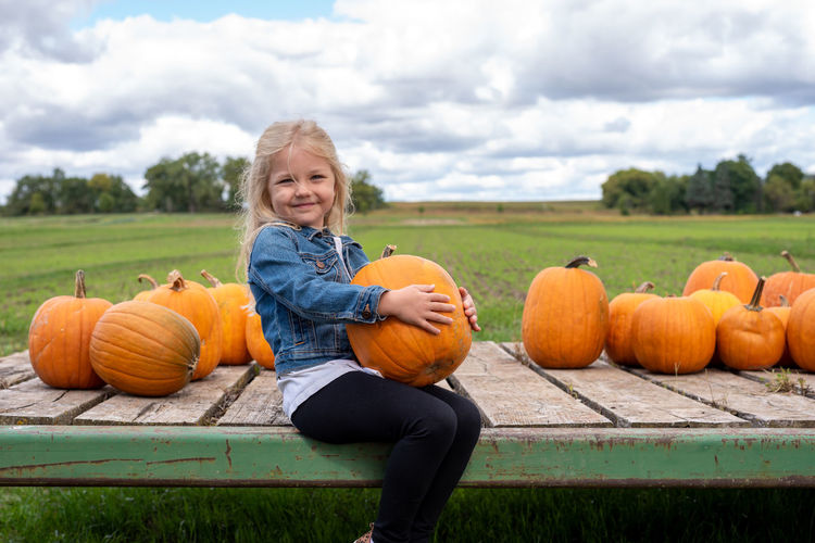 Portrait of smiling girl by pumpkins on field against sky