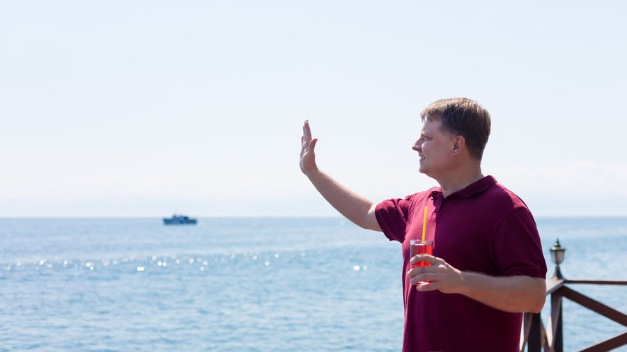 Side view of young man looking at sea against clear sky