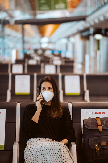 Woman wearing mask talking on phone while sitting at airport
