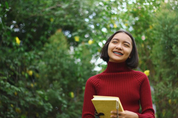 Smiling girl looking away while standing against tree