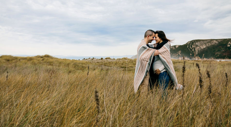 Pregnant woman with man standing on field against sky