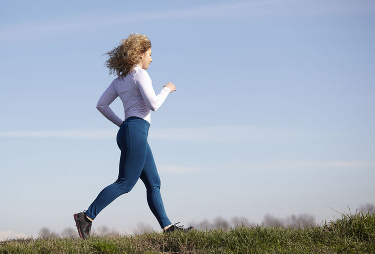 Full length of woman running on field against blue sky