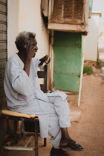 Vintage style photo of an old man using a phone while sitting on a chair 