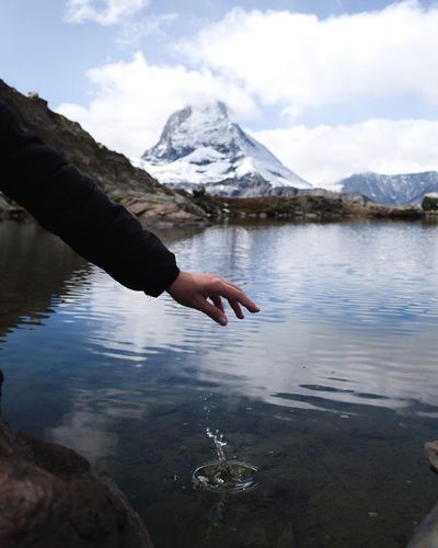 Close-up of person hand on lake against sky