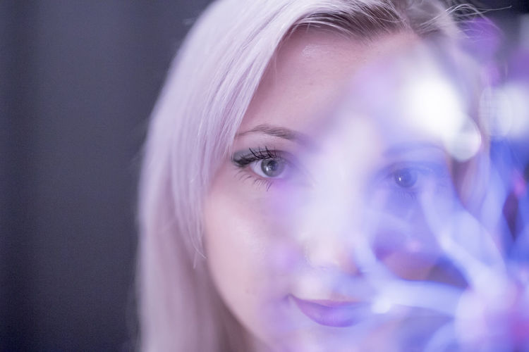 Close-up portrait of young woman holding plasma ball over black background