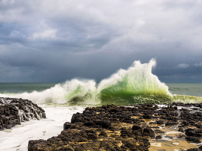 Waves splashing in sea against cloudy sky