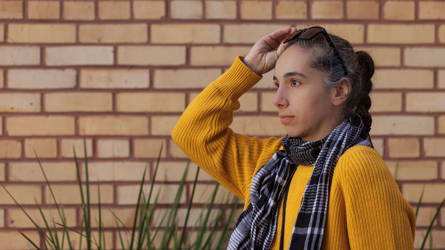 Woman looking away while standing against brick wall