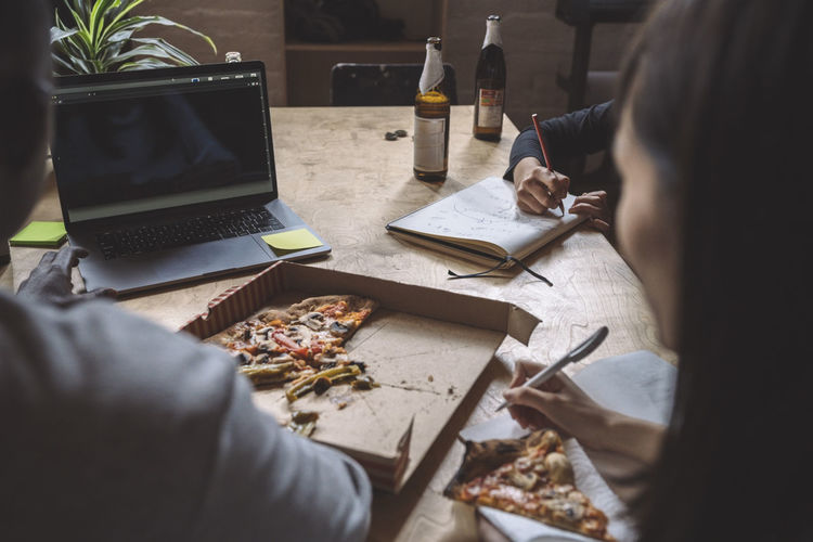 Coworkers working over coding while eating pizza at workplace