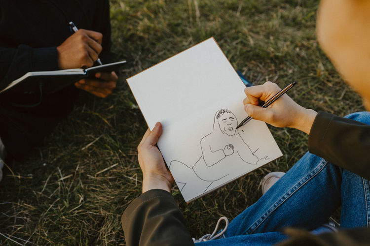 Cropped image of man's hands sketching in book at park
