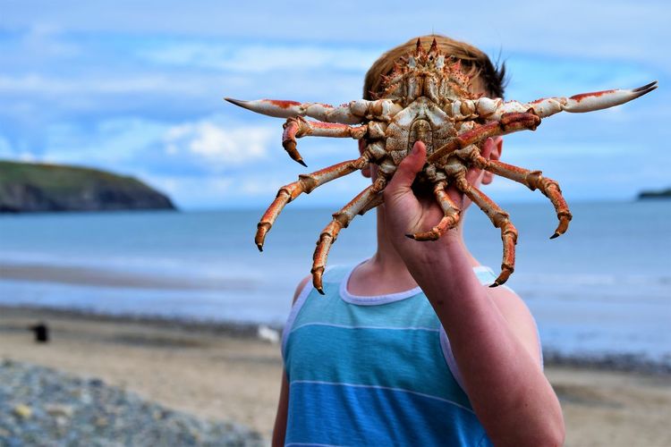 Teenage boy showing crab while standing at beach