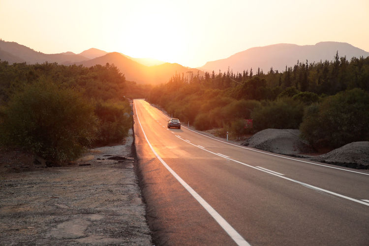 Road leading towards mountain against sky during sunset