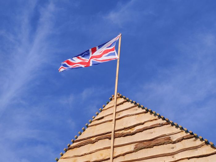 Low angle view of british flag and roof against blue sky