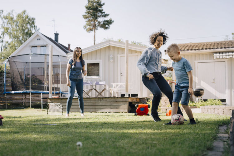 Mother and son playing soccer while woman standing in backyard