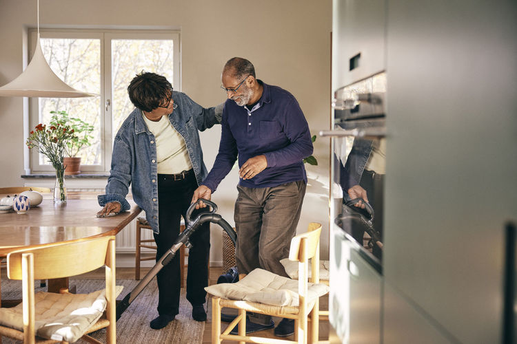Senior woman talking to man cleaning home with vacuum cleaner