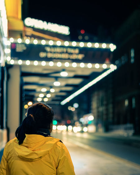 Rear view of woman standing on illuminated road at night