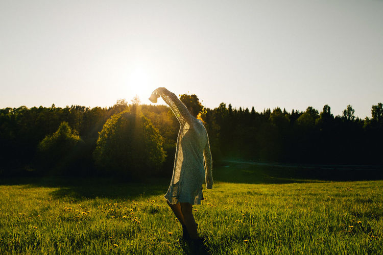 Side view of a woman dancing on a field against clear sky.