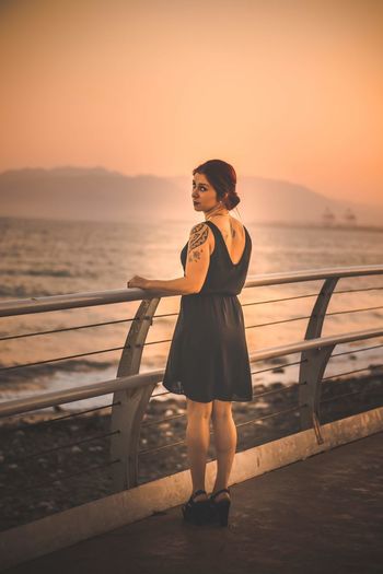 Portrait of woman standing at promenade against clear orange sky
