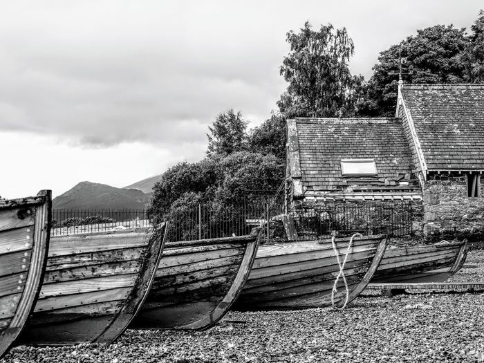 Abandoned rowboats moored on land against houses