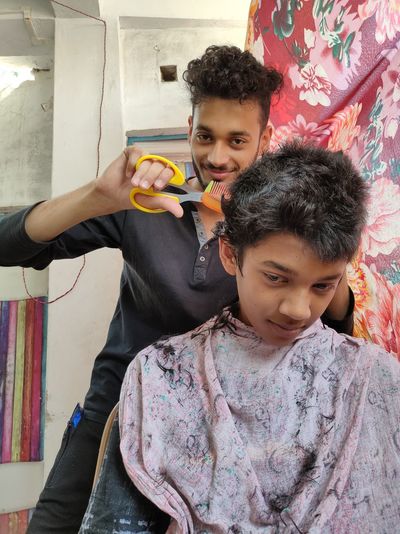 Low angle portrait of man cutting boy hair in salon