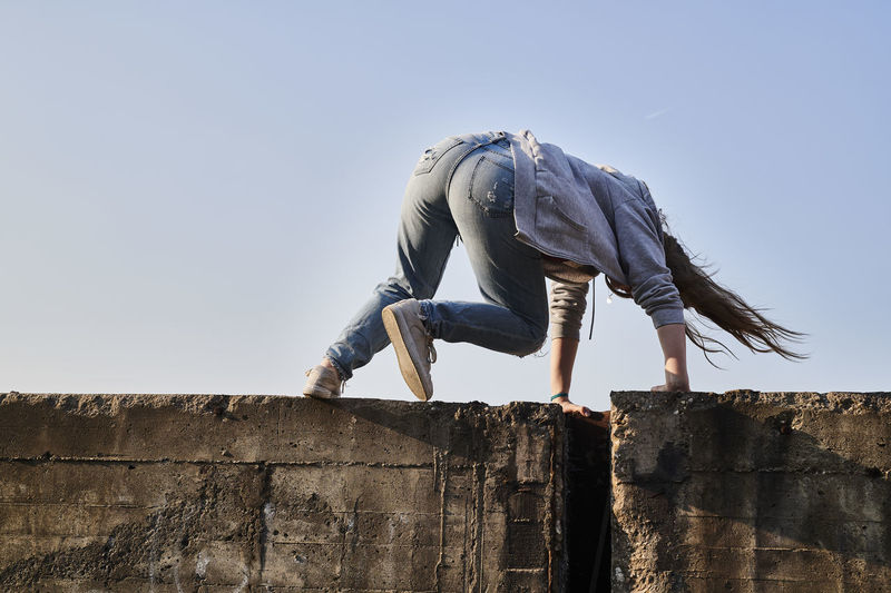 Young woman jumping over concrete wall, rear view
