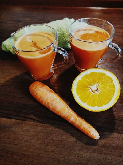 High angle view of carrot and orange by juice on wooden table