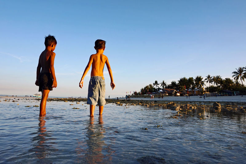 Rear view of shirtless friends standing in sea