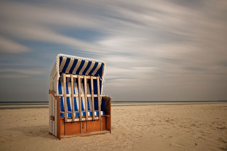 Hooded chair on beach against cloudy sky