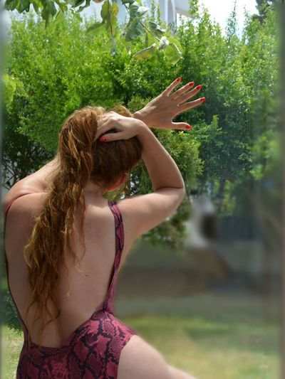 Rear view of woman wearing swimwear while sitting against trees