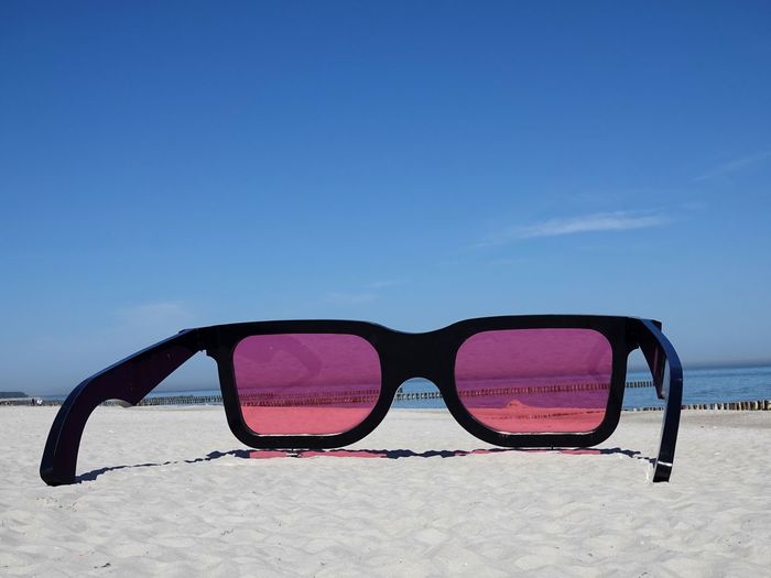 Sea see through sunglasses on beach against blue sky