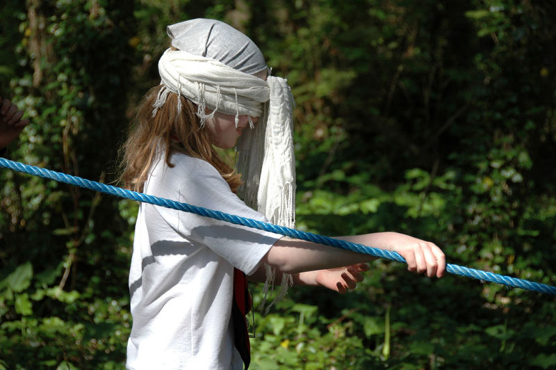 Side view of blindfolded girl walking while holding rope at park
