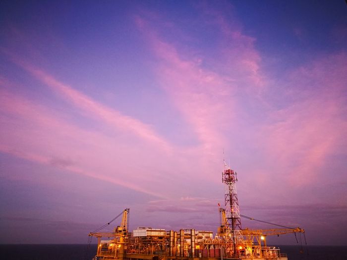 Illuminated offshore platform against sky at sunset