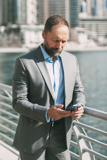 Businessman using mobile phone while standing by railign