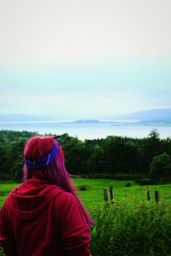 Rear view of woman with long dyed pink hair on grassy field against sky