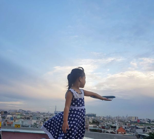 Optical illusion of girl holding airplane against sky during sunset