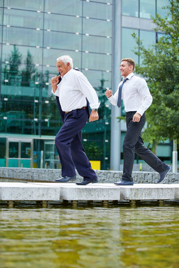 Full length of businessmen running on footbridge over lake