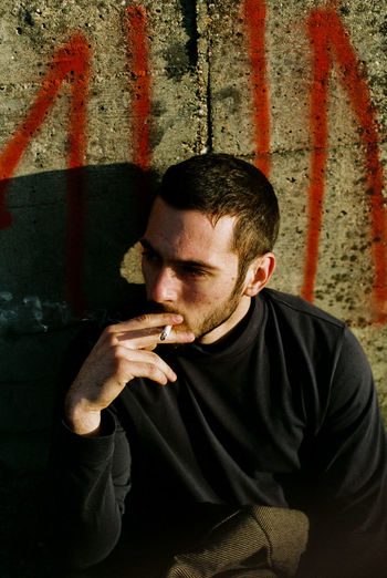 Young man smoking cigarette against wall