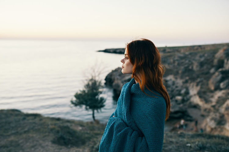 Side view of woman standing by sea against sky