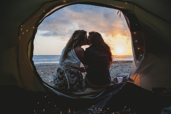 Lesbian couple kissing in tent at beach during sunset