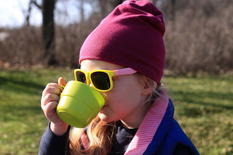 Smiling child in colorful clothes drinking tea from green reusable cup. eco-friendly family picnic.