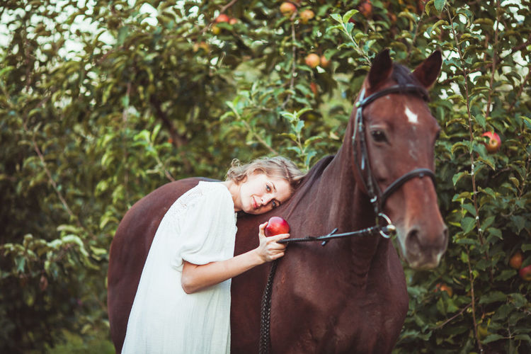 Portrait of woman holding apple standing by horse