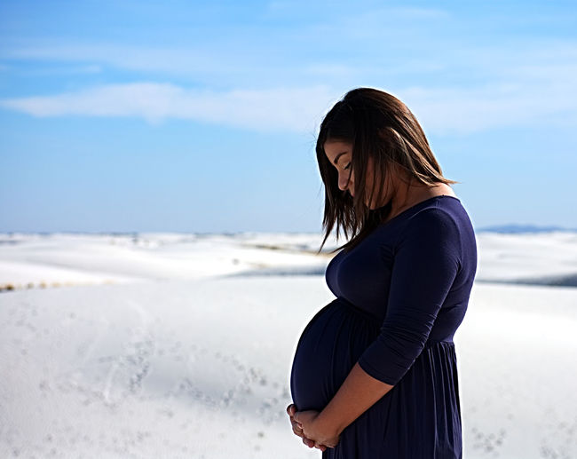 Side view of pregnant woman standing at beach against sky