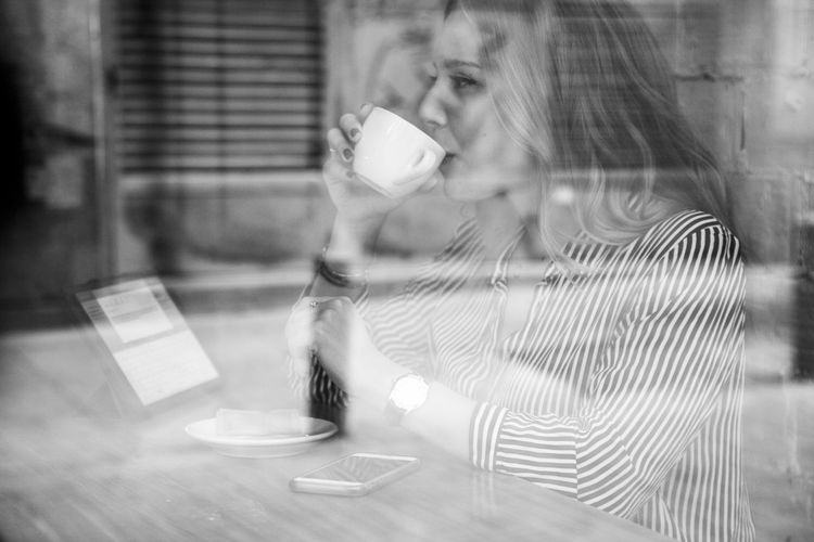 Woman drinking coffee in cafe seen through window
