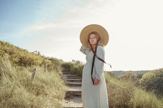 Rear view of woman wearing hat standing on field against sky