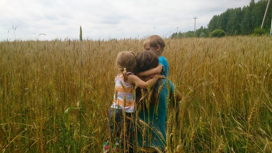 Rear view of mother embracing children amidst plants on field