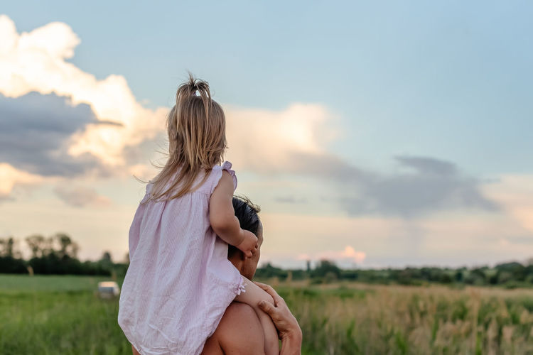 Rear view of man and little girl standing against sky during sunset